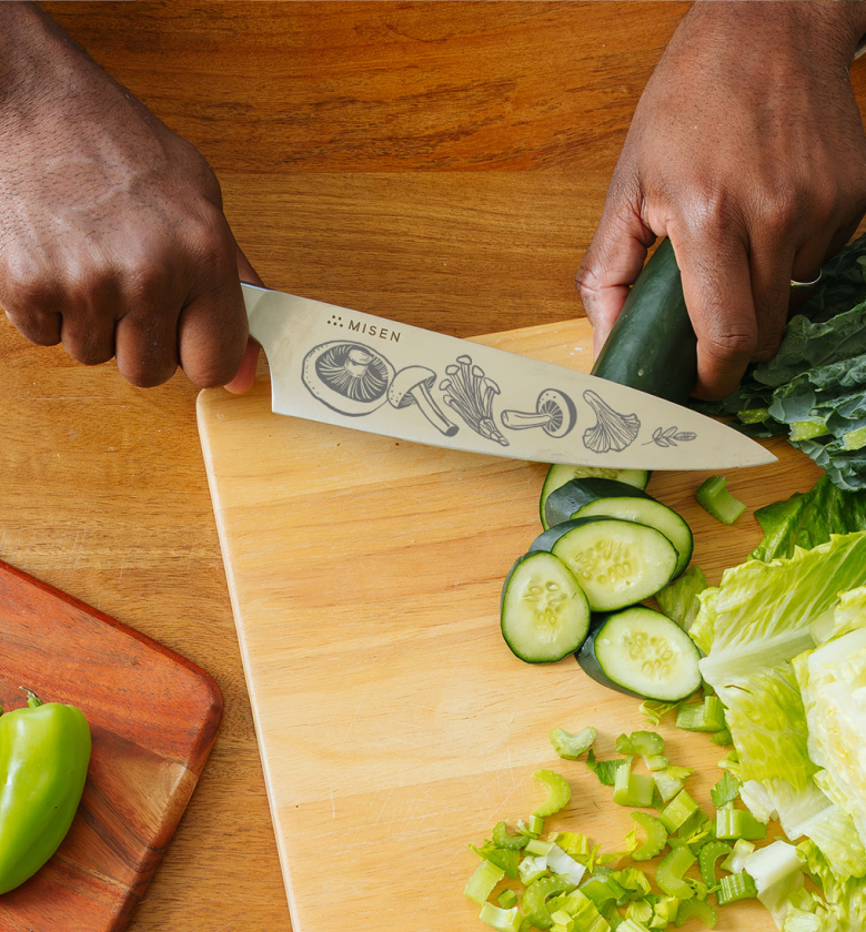 Misen chef's knife with mushroom etching slicing cucumber on wooden cutting board